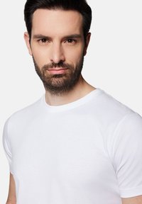 Biała bawełniana koszulka z okrągłym dekoltem, krótkimi rękawami i gładką teksturą, na neutralnym tle.