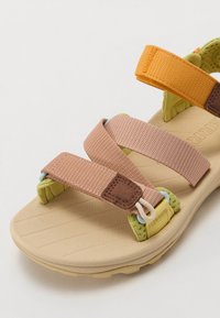 Flerfargede sandaler med tre justerbare tekstilremmer i rosa, brunt og oransje på en formet beige såle med teksturdetaljer.