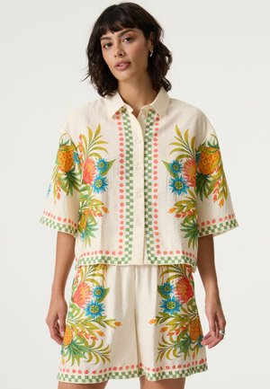 Kurzärmeliges, geknöpftes Blumenbluse und passender Rock aus cremefarbenem Stoff, mit lebhaften Farben, Ananas- und Blumenmustern und grünen Akzenten.