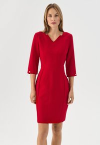 Rotes, eng anliegendes Kleid mit V-Ausschnitt, Dreiviertelärmeln, Eingrifftaschen an den Seitennähten und goldenen Knopfakzenten in der Nähe der Bündchen. Glatte Stoffoberfläche.
