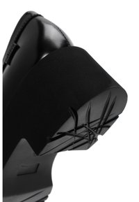Scarpa in pelle verniciata nera con una suola in gomma nera spessa, dotata di un fondo testurizzato per garantire aderenza e un design curvo e liscio nel tallone.