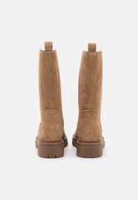 Hnědé semišové kozačky po kolena s hladkým povrchem, opatřené dekorativními perforacemi, silnými gumovými podrážkami a zadními poutky pro snadné obouvání.