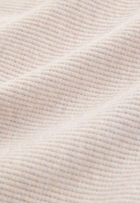 Lichtbeige stof met een getextureerd, geribbeld patroon, zacht gedrapeerd om diepte en subtiele variaties in kleur en textuur te tonen.