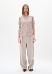 Satiini, mauve-väri blouse, jossa on lyhyet puffihihat ja V-pääntie, yhdistettynä vaalean taupe-värisiin leveisiin housuihin ja eläinkuosilla varustettuihin korkokenkiin.