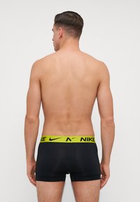 Czarne slipki boxerki z żółtym paskiem z logo Nike. Gładki materiał, dopasowany krój, średni stan i brak wyraźnych wzorów lub akcentów.