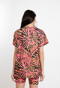 Yli suuri t-paita, jossa on kirkas tye-dye-kuvioina pinkkiä, oranssia ja keltaista mustalla taustalla. Lyhyet hihat ja pyöreä kaula-aukko.