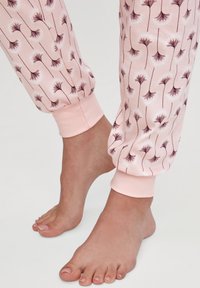 Lichtroze joggers met een paardenbloemprint, voorzien van elastische boorden en een zachte textuur. Close-up weergave met voeten en been details.