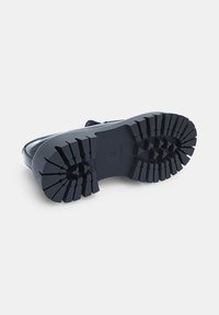 Suela de bota de goma negra con profundas bandas de tracción, con forma curvada y un diseño robusto para una mejor agarre y durabilidad.