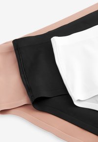 Drei nahtlose Unterwäscheteile in Beige, Schwarz und Weiß, übereinander gestapelt auf einer weißen Oberfläche.