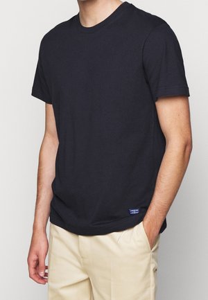 Schwarzes Baumwoll-T-Shirt mit Rundhalsausschnitt und kurzen Ärmeln. Enthält ein kleines blaues Etikett am unteren linken Rand. Glatte Textur, lockere Passform.