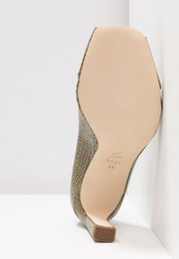 Talons hauts en cuir vert avec un motif texturé en peau de serpent ; semelle beige lisse avec un léger talon et logo embossé au fond.