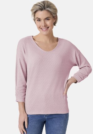 Helles rosa Strickoberteil mit einem strukturierten Muster, ausgestattet mit einem weiten Ausschnitt und langen Ärmeln, kombiniert mit blauen Jeans.