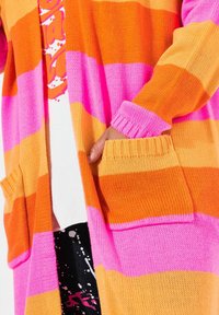 Cardigan a righe arancioni e rosa con polsini e tasche a costine, realizzato in tessuto knit testurizzato, caratterizzato da un design aperto e rilassato.