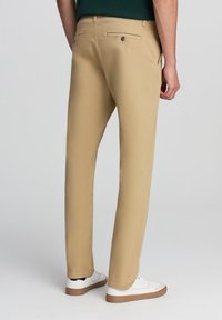 Beżowe bawełniane spodnie o slim fit, z dwiema tylnymi kieszeniami zapinanymi na guziki i podwiniętymi nogawkami. Noszone z białymi trampkami.