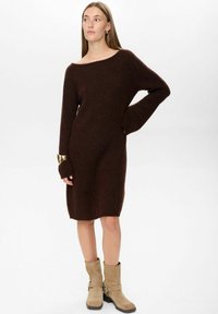 Rochie tricotată maro, cu decolteu off-the-shoulder și mâneci lungi; asortată cu botine bej până la gleznă, cu detalii cu cataramă.