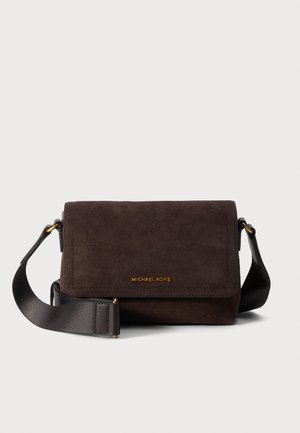 Bolso bandolera de ante marrón oscuro con solapa, correa negra ancha ajustable y pequeño logotipo dorado "Michael Kors" en la parte delantera.