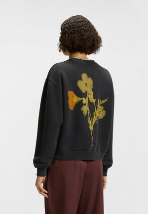Zwarte sweatshirt met een groot bloemmotief in geel en oranje op de achterkant, met geribbelde boorden en zoom, en een relaxte pasvorm.
