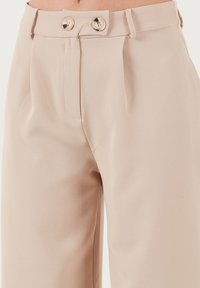 Beige tailored trousers in lightweight fabric, featuring a high waist, dual button closure, and front pleats for structure and style.