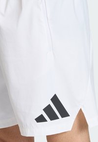 Λευκά αθλητικά σορτς από ελαφρύ ύφασμα, με μαύρο τριγωνικό λογότυπο στο κάτω αριστερό μέρος και τσέπη με φερμουάρ.