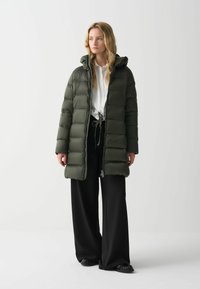 Fyllig olivgrön parka-jacka med huva, dragkedja fram, quiltat mönster och sidofickor, matchad med svarta vida byxor och svarta skor.