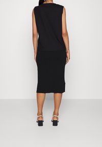 Black sleeveless top and mid-length skirt, both in a smooth, stretchy fabric. Footwear features block heels and thin ankle straps.