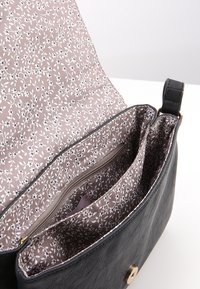 Borsa in pelle nera aperta per mostrare molteplici scomparti con foderatura in tessuto floreale marrone chiaro e una tasca con zip all'interno.