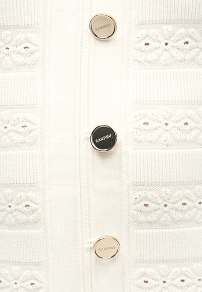 Λευκό πλεκτό ύφασμα με υφασμένα διαμάντι μοτίβα και τρία στρογγυλά χρυσά κουμπιά με χαραγμένο το "SANDRO" σε κατακόρυφη διάταξη.