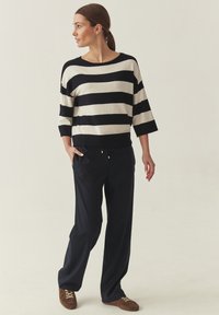 Pull rayé crème et marine, manches larges. Associé à un pantalon ample marine, avec ceinture élastique et cordon doré. Chaussures en daim marron.