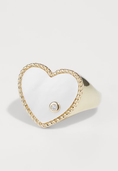 Kuldne südamekujuline sõrmus keerdpärga piiriga, läikiv valge emailpind ja väike bezel-seatud teemandi aksent.