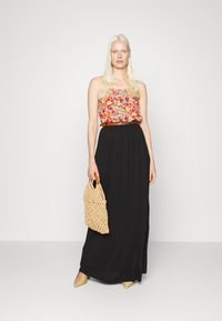 Top cropped floral com efeito franzido, saia maxi preta, bolsa de palha bege e sapatos slip-on claros com bico fino.