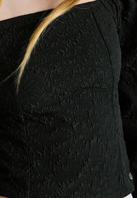 Top nero con un motivo floreale testurizzato, design off-the-shoulder e maniche corte, con una forma aderente e dettagli hardware minimi.