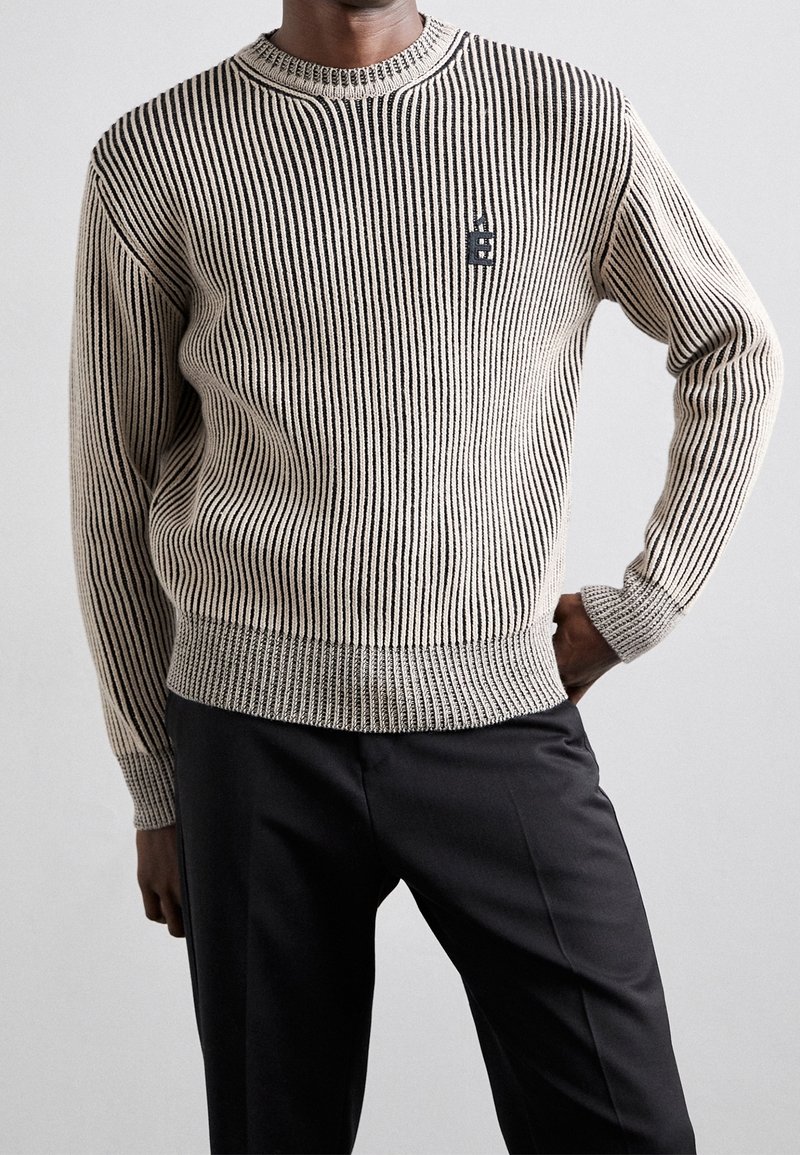 Gestrickter Pullover mit vertikalen schwarzen und beigen Streifen, rundem Hals und gerippten Bündchen. Hat ein kleines schwarzes Logo auf der Brust.