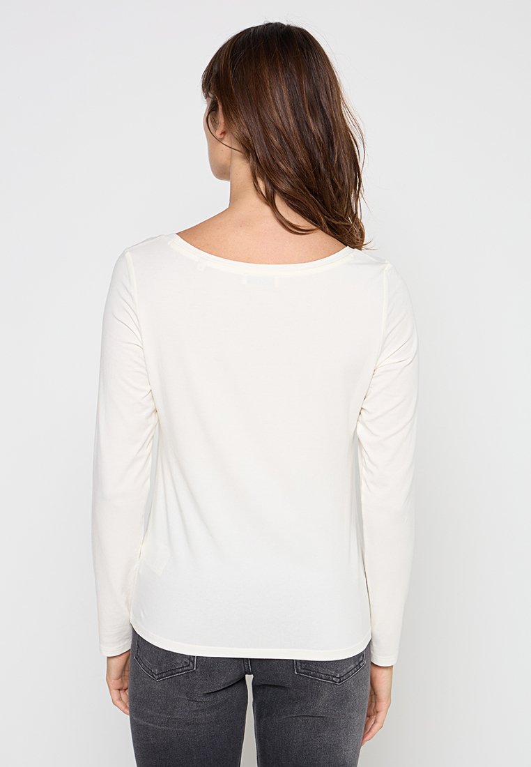 Langärmliges cremefarbenes Oberteil aus weichem Stoff mit rundem Halsausschnitt und geschwungenem Saum, das eine glatte Textur und ein einfaches Design aufweist.