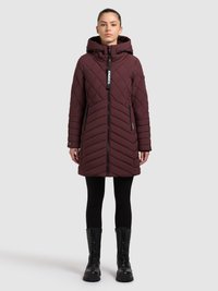 Geacă matlasată visinie cu glugă, fermoar frontal și model în formă de chevron. Purtată peste colanți negri și cizme negre masive.