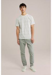 Tricou cu mânecă scurtă în nuanță de crem cu dungi orizontale negre, asortat cu pantaloni verzi deschiși și adidași albi. Design simplu și casual.