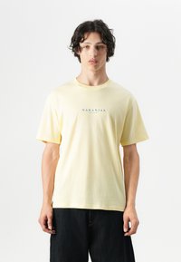 T-shirt di cotone gialla con maniche corte, presenta il testo blu "NARANJAS" centrato nella parte anteriore. Vestibilità casual con una texture morbida.