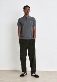 Graues Polohemd, dunkelgrüne Cordhosen, schwarz-weiße Sneaker, Stehpose. Einfaches Design, einfarbige Farben, lässiger Look.
