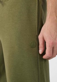Olijfgroene joggingsbroeken van een zachte katoenmix, met een slim fit, gestikte details en een ronde logo-patch op de linker bovenben.