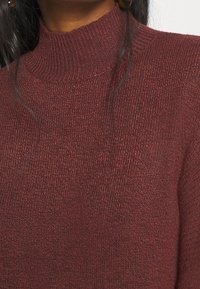 Maglione a collo alto bordeaux realizzato in tessuto a maglia testurizzata, con colletto a costine aderente e un aspetto morbido e caldo.
