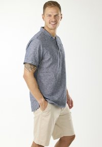 Kortärmad skjorta med krage i melerat blått tyg, tillsammans med ljusbeige shorts. Har en bröstficka och avslappnad passform.