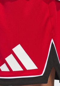 Röda sportshorts i andningsbart meshtyg, med en vit design i tre ränder och svart kant vid fållen.