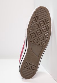 Red suede sneaker sole with textured brown rubber tread, white toe cap, and black side stripe. Features a geometric pattern on the sole.