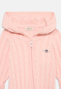 Rosa kabelstrikket zip-up hettegenser med hette, med et lite GANT-logo-patch og en myk tekstur. Glidelåsen er sentral, og ermene er ribbestrikket.