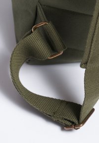 Correa de lona verde oliva con una textura tejida, que cuenta con una hebilla metálica para ajuste y sujeción a una bolsa o accesorio.