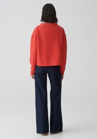 Pull rouge côtelé au design court, associé à un jean large bleu foncé. La texture est lisse avec des lignes verticales marquées.