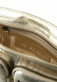 Interno della borsa metallica argento con una tasca con zip, texture liscia e rivestimento beige con marchio in rilievo.