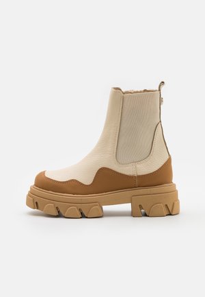 Beige støvle med højt skaft, tekstureret læder, elastisk sidepanel, brun læderkant og robust, grov sål.