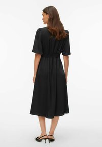 Vestido midi negro con mangas cortas abullonadas, cintura elástica, falda fluida, textura suave y diseño minimalista.