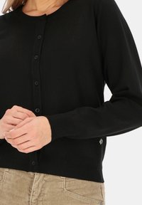 Czarny kardigan wykonany z miękkiego dzianinowego materiału, z guzikami z przodu, długimi rękawami oraz małym detalem logo blisko dolnego szwu.