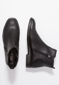 Botines de cuero negro con cierre de cremallera, puntera redonda y un tacón bajo en bloque. Textura suave y diseño minimalista.